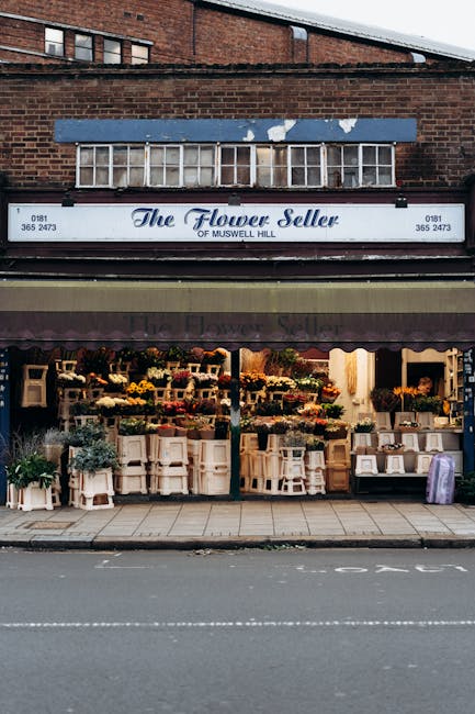 The Flower Seller shopfront on Muswell Hill features a display of vibrant floral arrangements arranged on white shelving units and tables outside the store. The flowers include a variety of lilies, ro